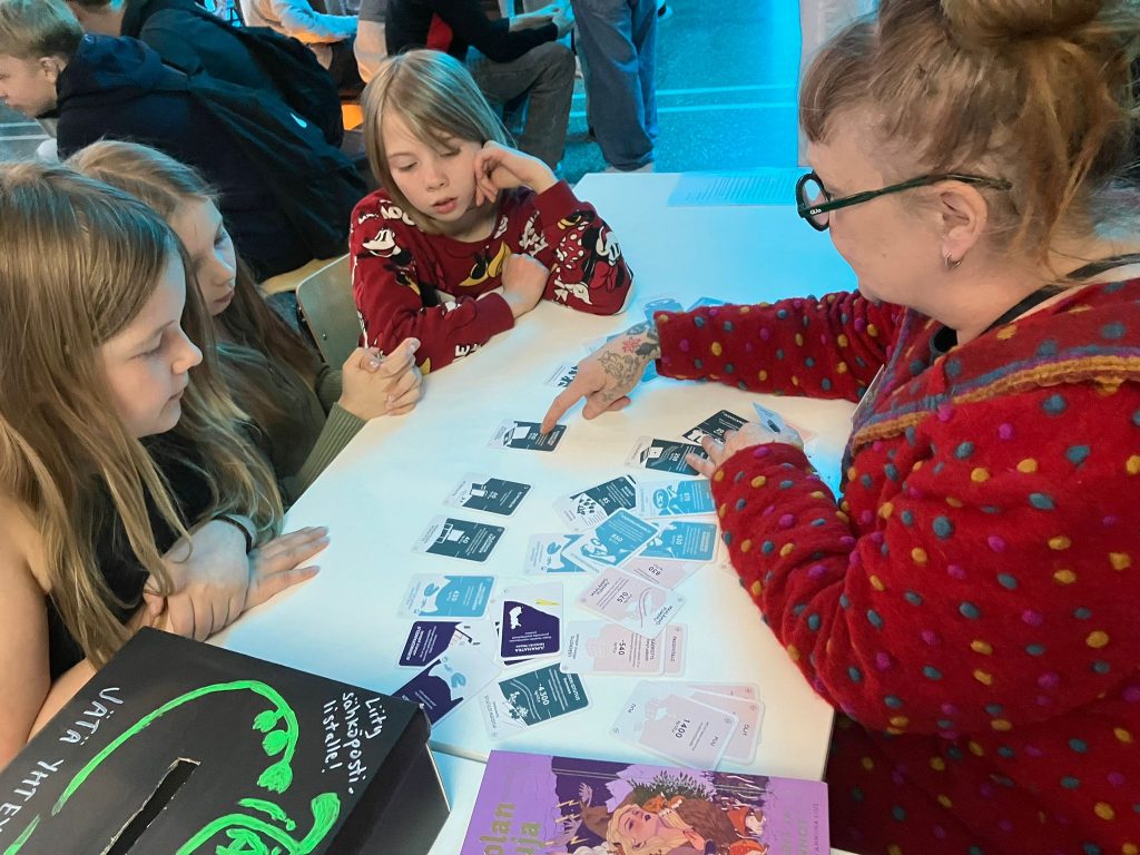 Beteendepsykolog Sinikka Hynninen-Otva spelar Klimatkoll (Ilmastotietäjä) med elever under Sci Fest-mässan i Joensuu, maj 2025.