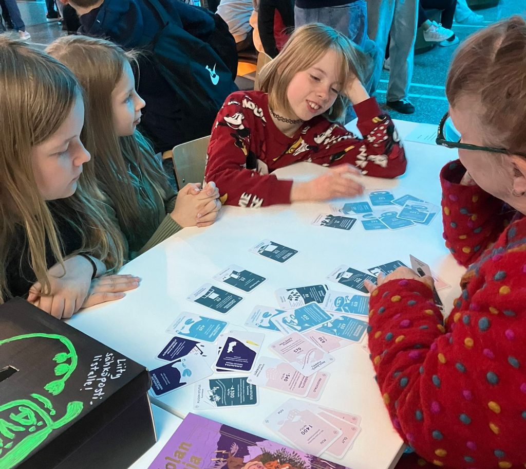Beteendepsykolog Sinikka Hynninen-Otva spelar Klimatkoll (Ilmastotietäjä) med elever under Sci Fest-mässan i Joensuu, maj 2025.